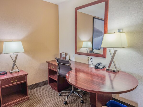 Ein Hotelzimmer mit einem Holztisch, zwei Lampen, einem Stuhl, einem Spiegel und einem Telefon.
