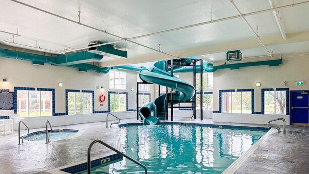 An indoor swimming pool with a spiral slide, clear poolside areas, and large windows.