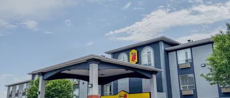 A hotel with a covered entrance, a sign reading "Super 8", and a clear blue sky with clouds.
