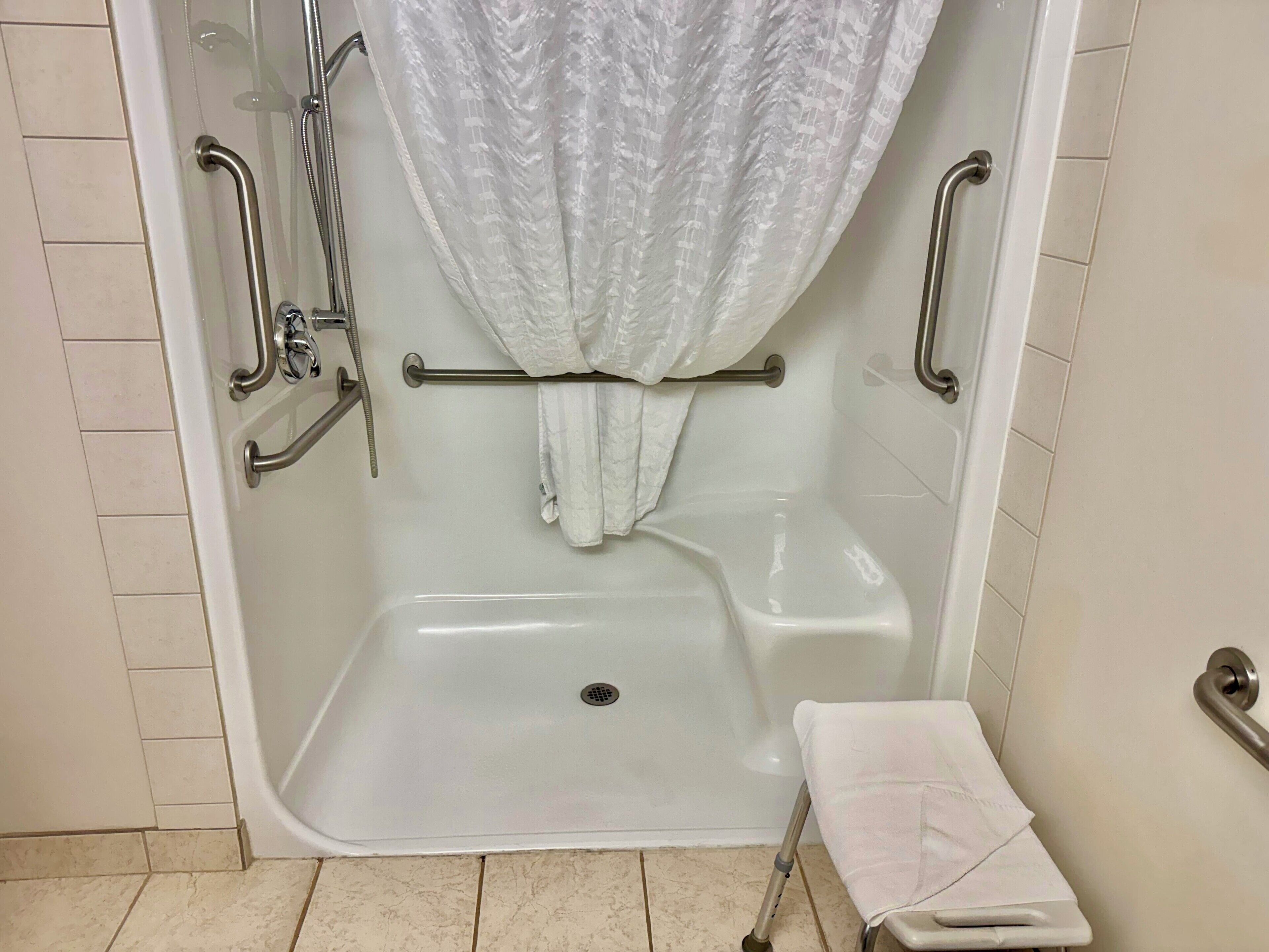 A walk-in shower with a grab bar, a shower curtain, and a small bench with a towel.
