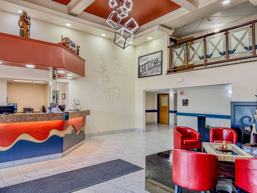 A hotel lobby with a reception desk, red chairs, a marble floor, and a staircase.