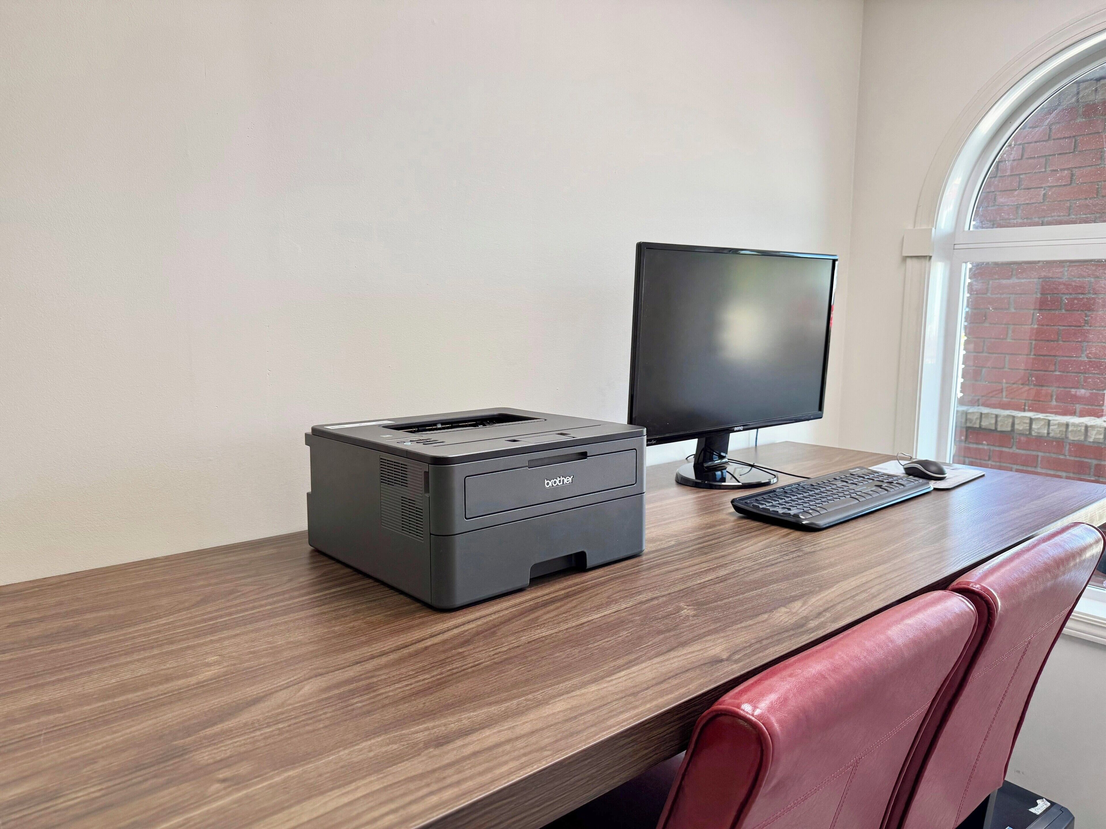 A workspace with a printer, monitor, keyboard, and mouse on a wooden desk.