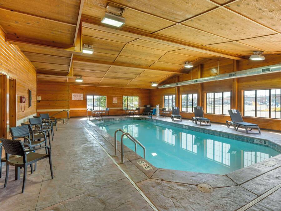Une piscine intérieure à l’eau claire, entourée de murs et d’un plafond en bois, avec des chaises longues et un sol carrelé.