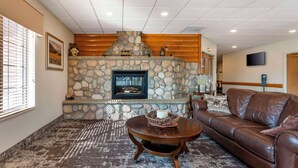 A cozy living room with a stone fireplace, leather sofa, and a coffee table. - Best Western Yellowstone Crossing (Laurel)