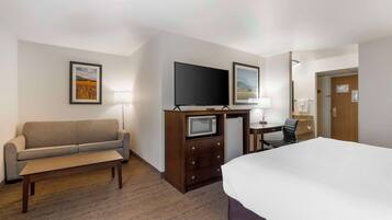 A hotel room with a bed, a sofa, a desk with a TV, a microwave, and a chair.