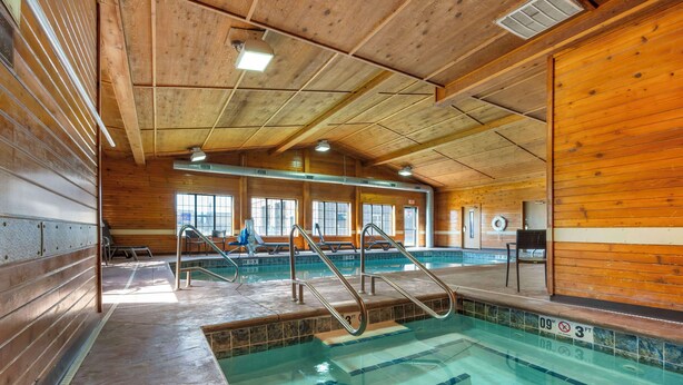 An indoor swimming pool with wooden walls and ceiling, clear water, and a lifeguard chair. - Best Western Yellowstone Crossing (Laurel)