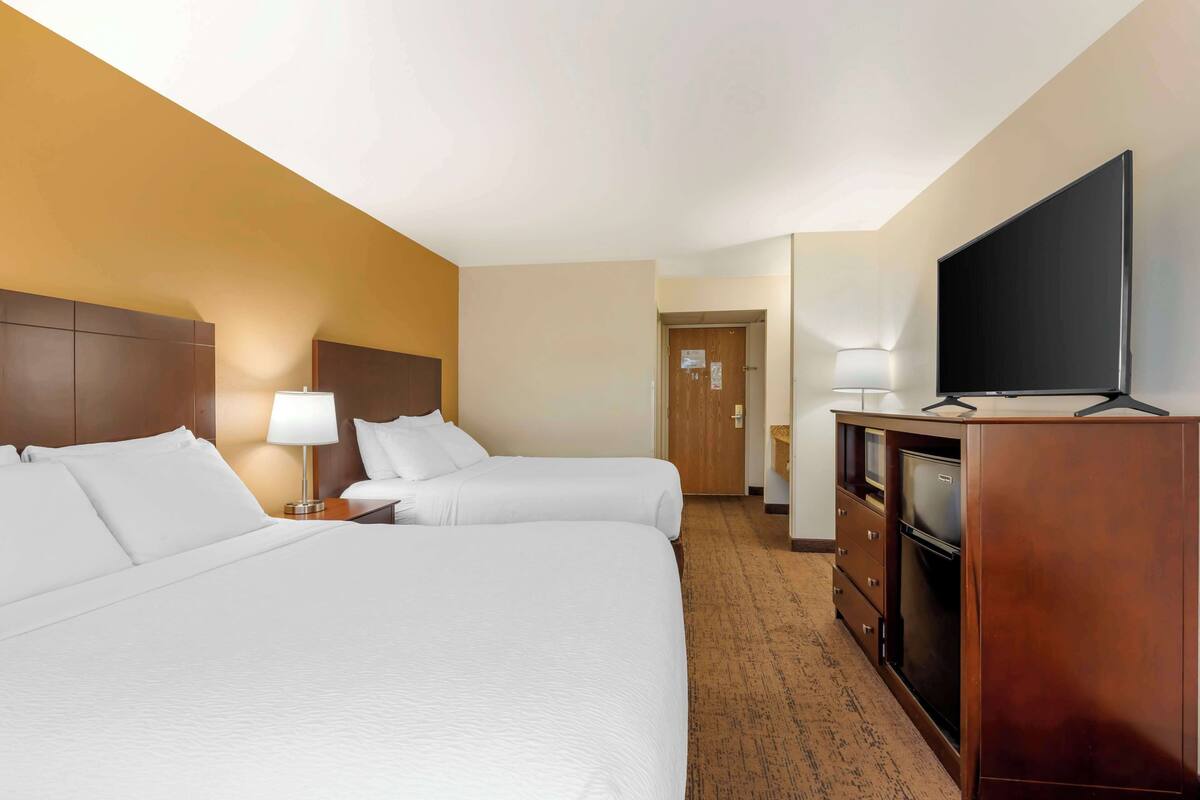 A hotel room with two beds, a TV, a dresser, and a door leading to another room.