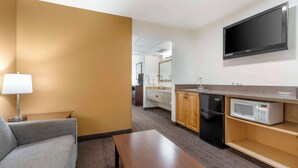 A compact hotel room with a sofa, a small table, a TV mounted on the wall, a microwave, and a compact kitchenette. - Best Western Yellowstone Crossing (Laurel)