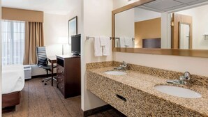 A hotel room with a bed, a desk with a chair, a TV, a double sink, and a large mirror. - Best Western Yellowstone Crossing (Laurel)