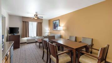 Habitación de hotel con comedor, televisión, ventilador de techo y ventana con cortinas.