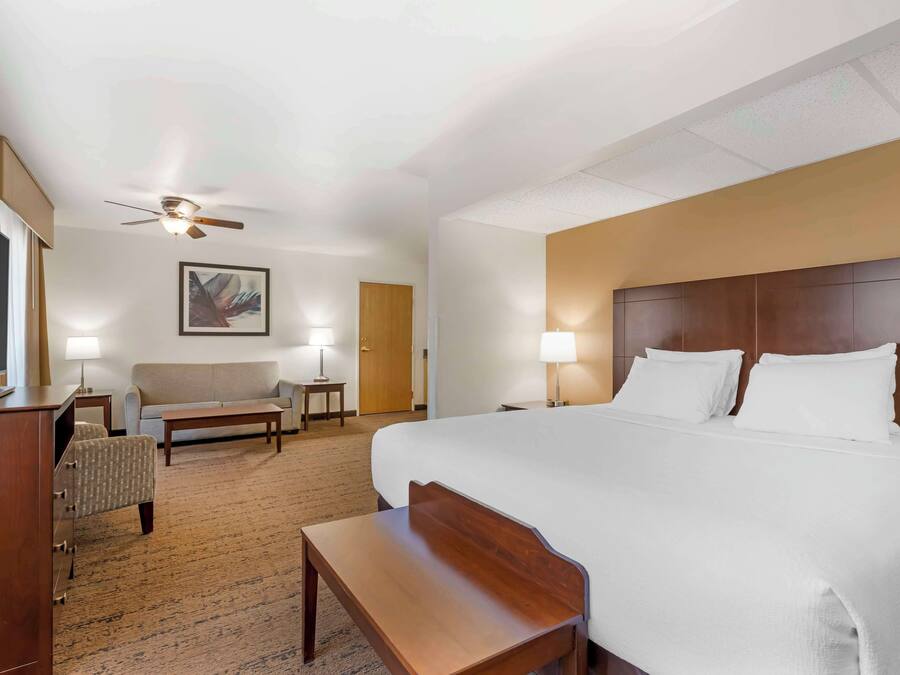 Een hotelkamer met een groot bed, een bureau, een stoel, een bank, een plafondventilator en een schilderij aan de muur.