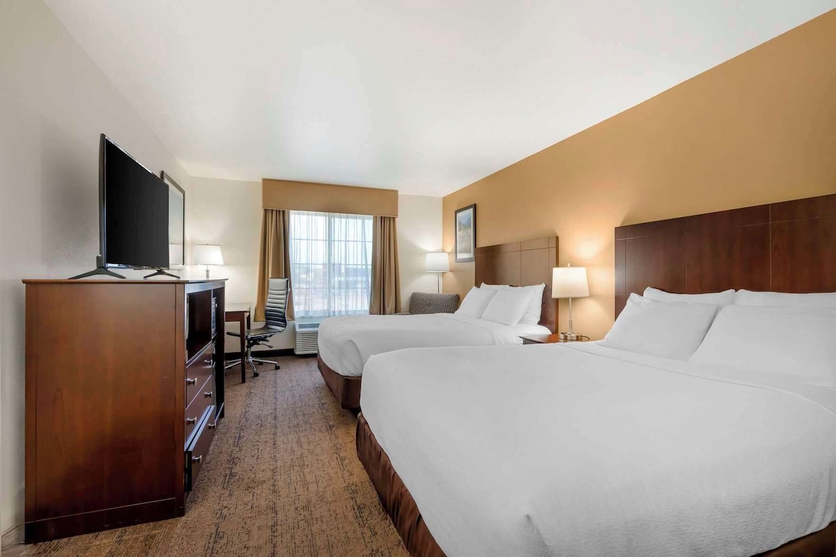 A hotel room with two beds, a TV, a desk, and a chair.