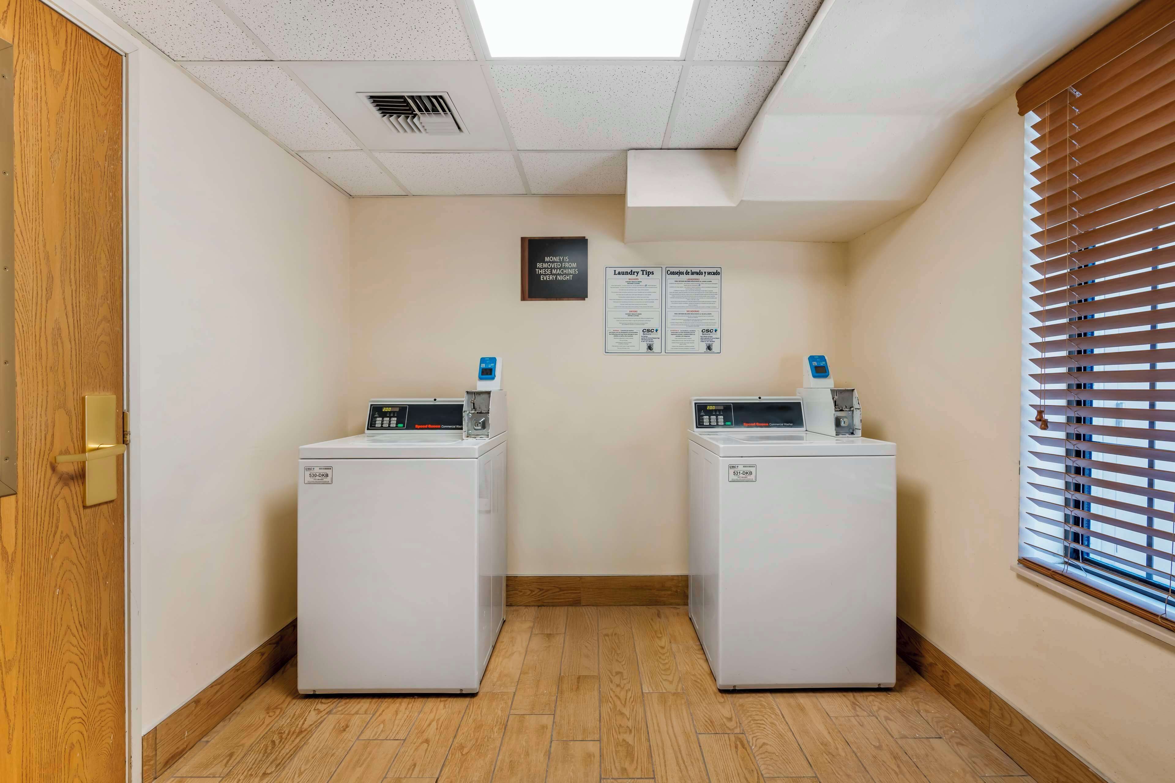 A laundry room with two front-loading washing machines, a ceiling vent, and a window with blinds.