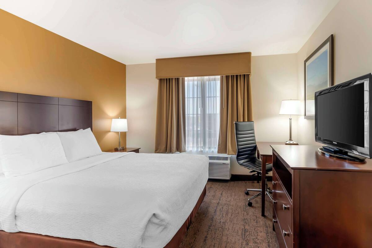 A hotel room with a large bed, a desk with a television, a chair, and a window with curtains.