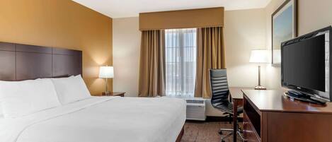 A hotel room with a large bed, a desk with a television, a chair, and a window with curtains.
