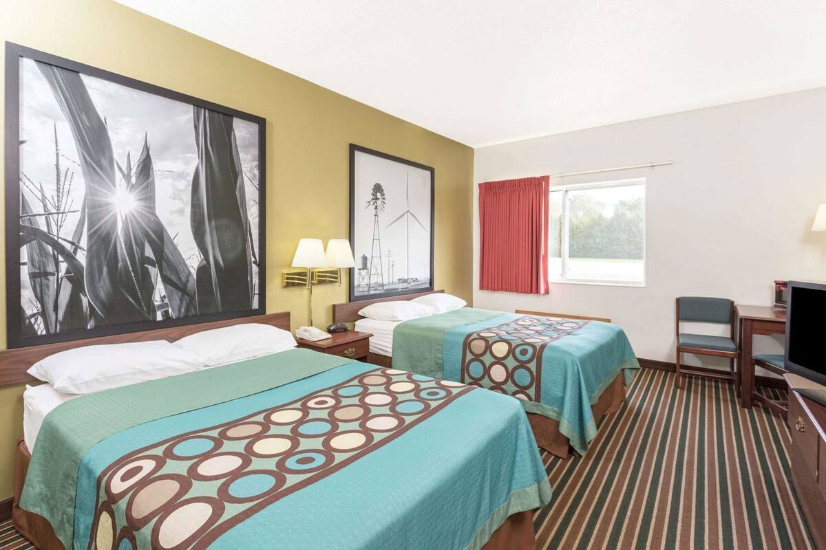A hotel room with two beds, a television, a desk, and a window with curtains.