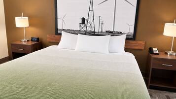 Habitación de hotel con una cama grande, dos mesitas de noche, un reloj, un teléfono y un cuadro colgado en la pared con aerogeneradores.