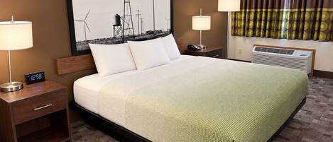 A hotel room with a large bed, two bedside tables, a wall clock, a window with curtains, and a wall-mounted air conditioner.