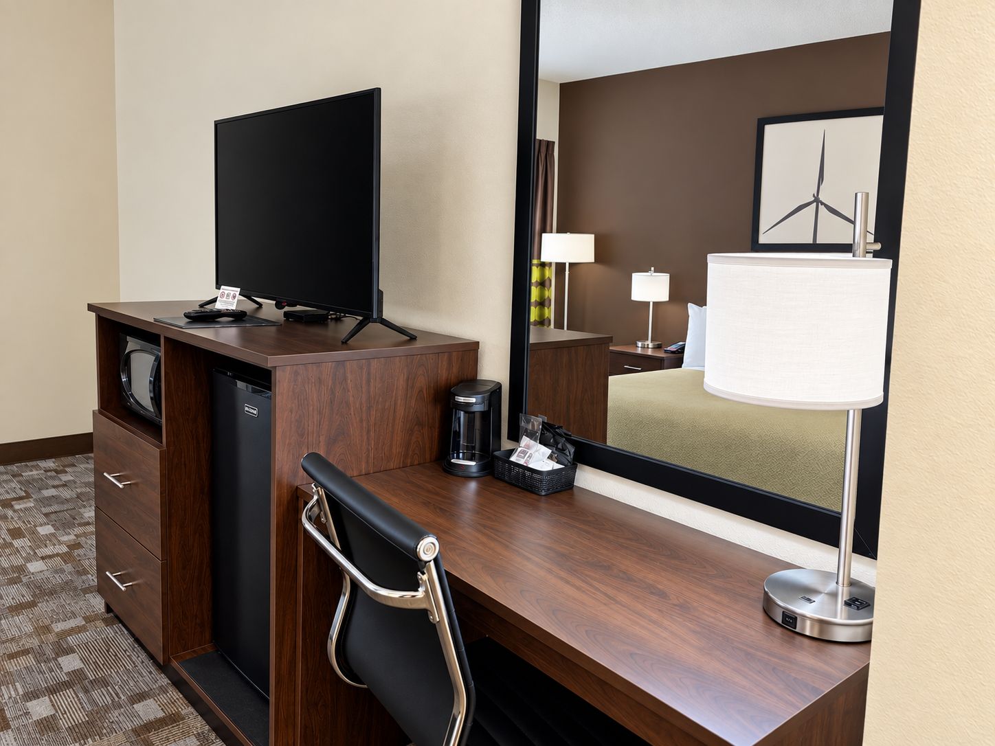 A hotel room with a desk, a television, a coffee maker, a lamp, and a bed.