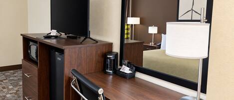 Una habitación de hotel con escritorio, televisión, cafetera, lámpara y cama.