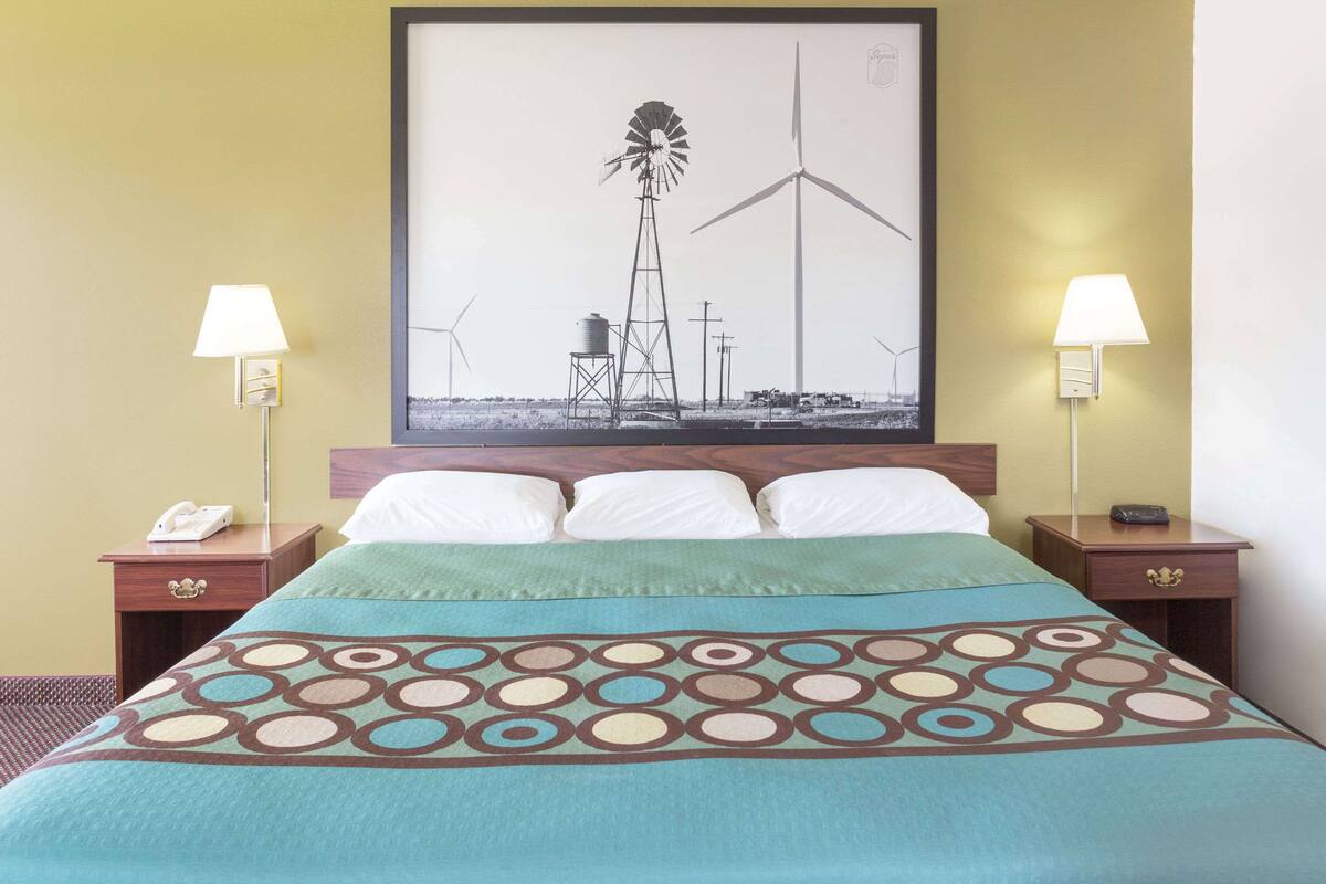 A hotel room with a bed, two bedside tables, a lamp on each table, a framed picture on the wall, and a telephone on one of the tables.