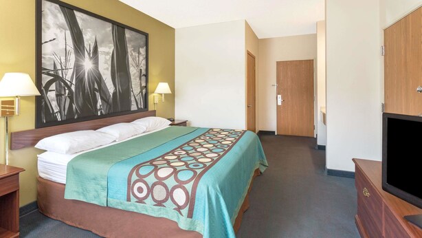 A hotel room with a bed, a TV, a painting on the wall, and a door in the background. - Super 8 by Wyndham Cresco IA (Cresco)