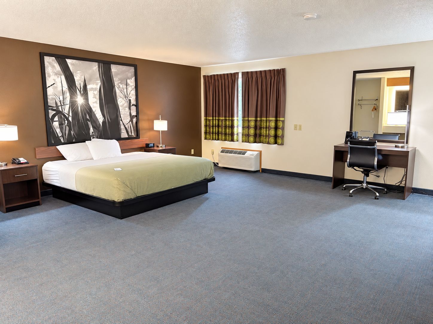 A hotel room with a bed, bedside table, lamp, desk, chair, and a large mirror.