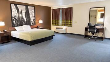 A hotel room with a bed, bedside table, lamp, desk, chair, and a large mirror.