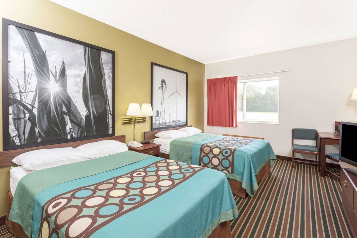 A hotel room with two beds, a TV, a desk, and a window with curtains.