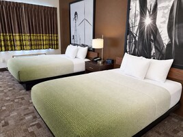 Habitación de hotel con dos camas, una mesita de noche, una lámpara y un cuadro de molinos.