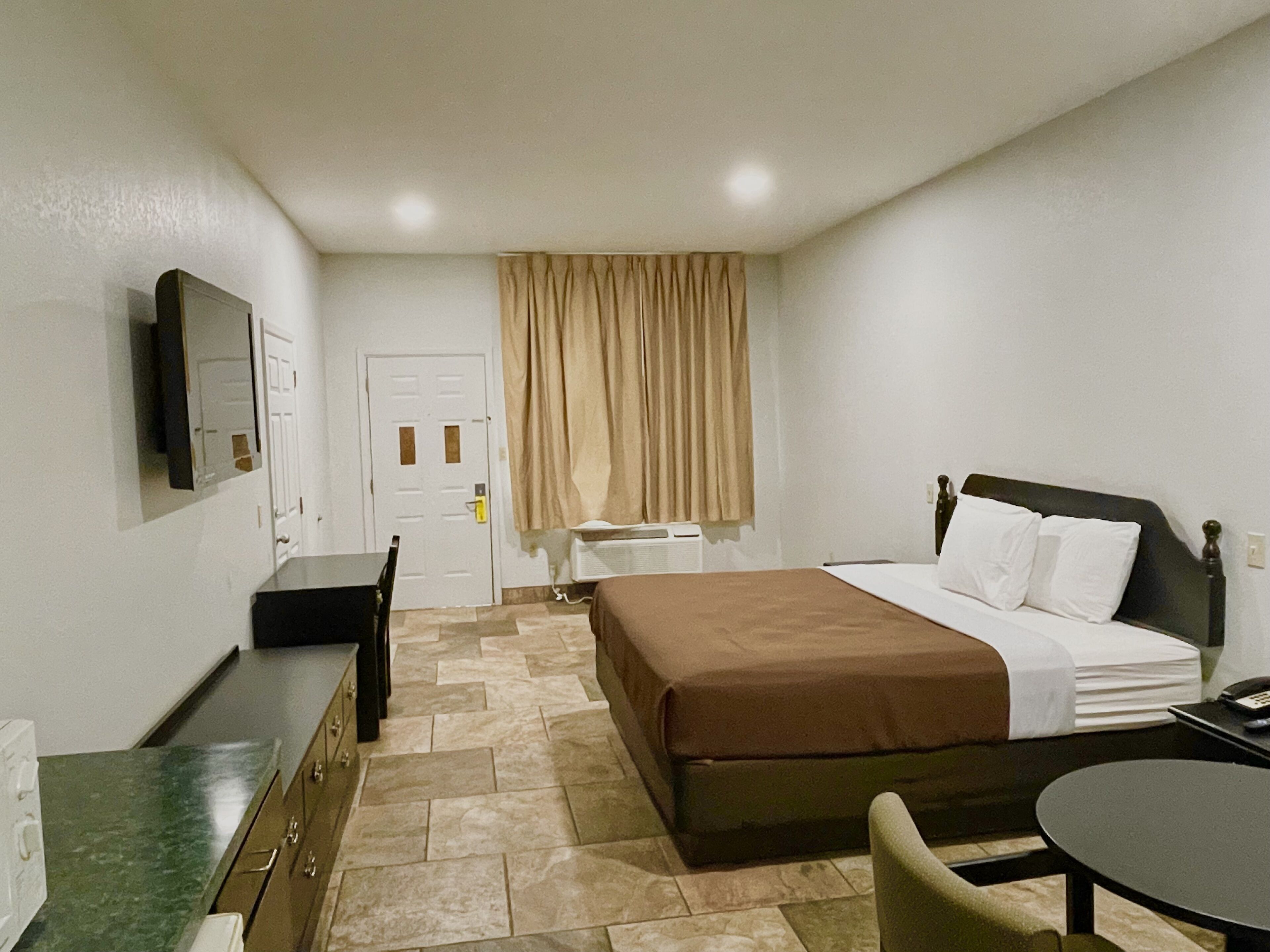 A hotel room with a bed, a desk, a chair, a television, and a window with curtains.