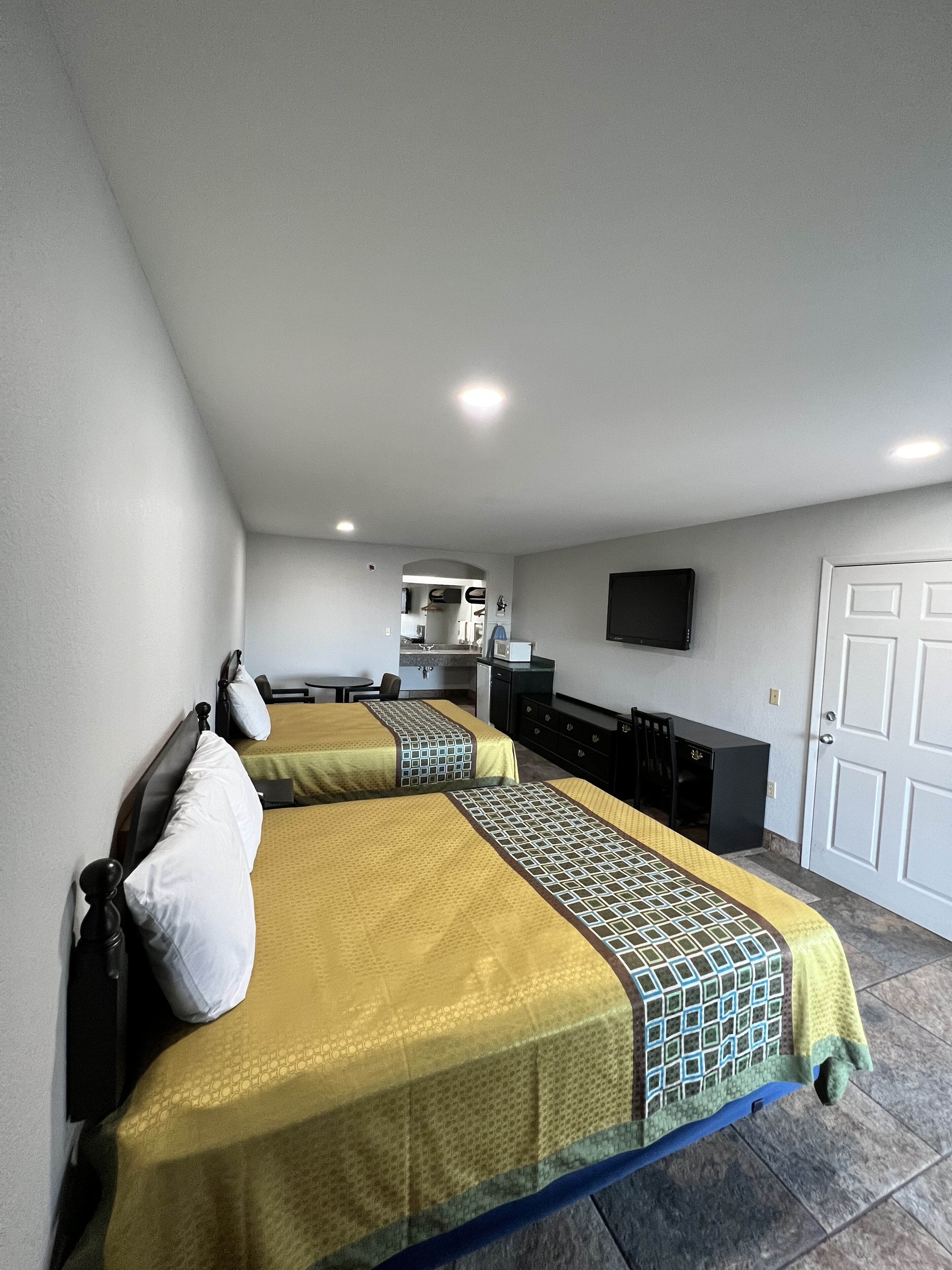 Habitación de hotel con dos camas, kitchenette, televisor de pantalla plana y una puerta.