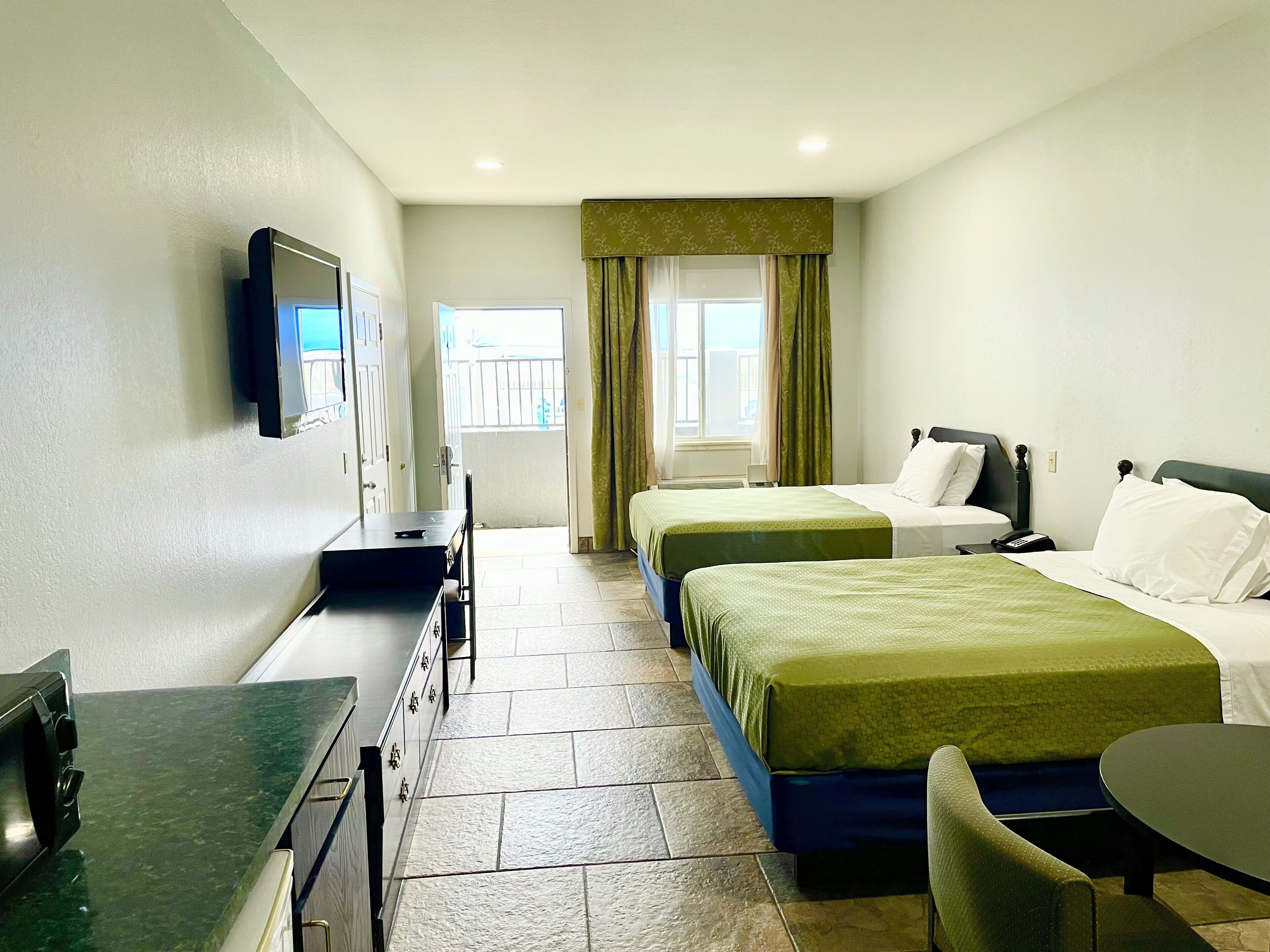 Habitación de hotel con dos camas, un escritorio, una silla, un televisor y una ventana con cortinas.