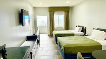 Habitación de hotel con dos camas, un escritorio, una silla, un televisor y una ventana con cortinas.