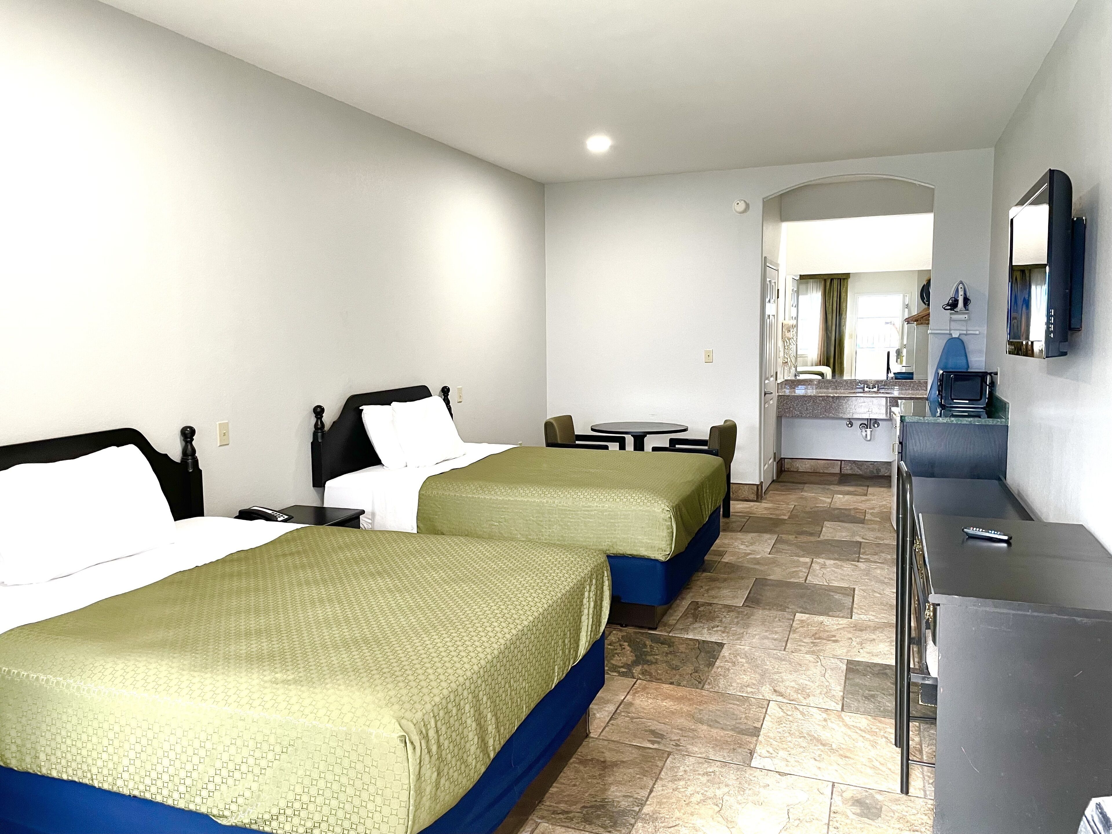 Une chambre d’hôtel avec deux lits, une petite table, un bureau, un miroir et un téléviseur.