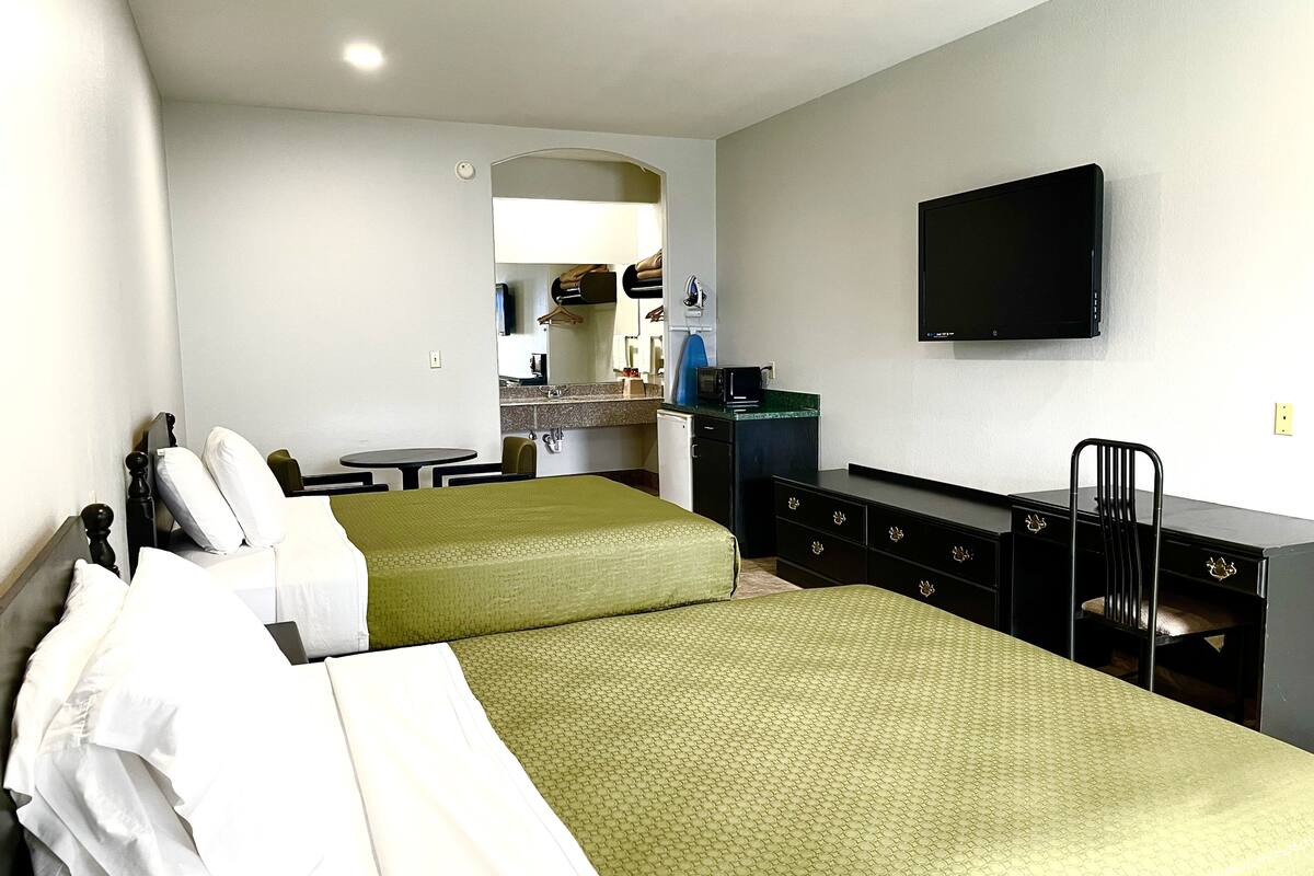 A hotel room with two beds, a desk, a chair, a television, and a kitchenette.