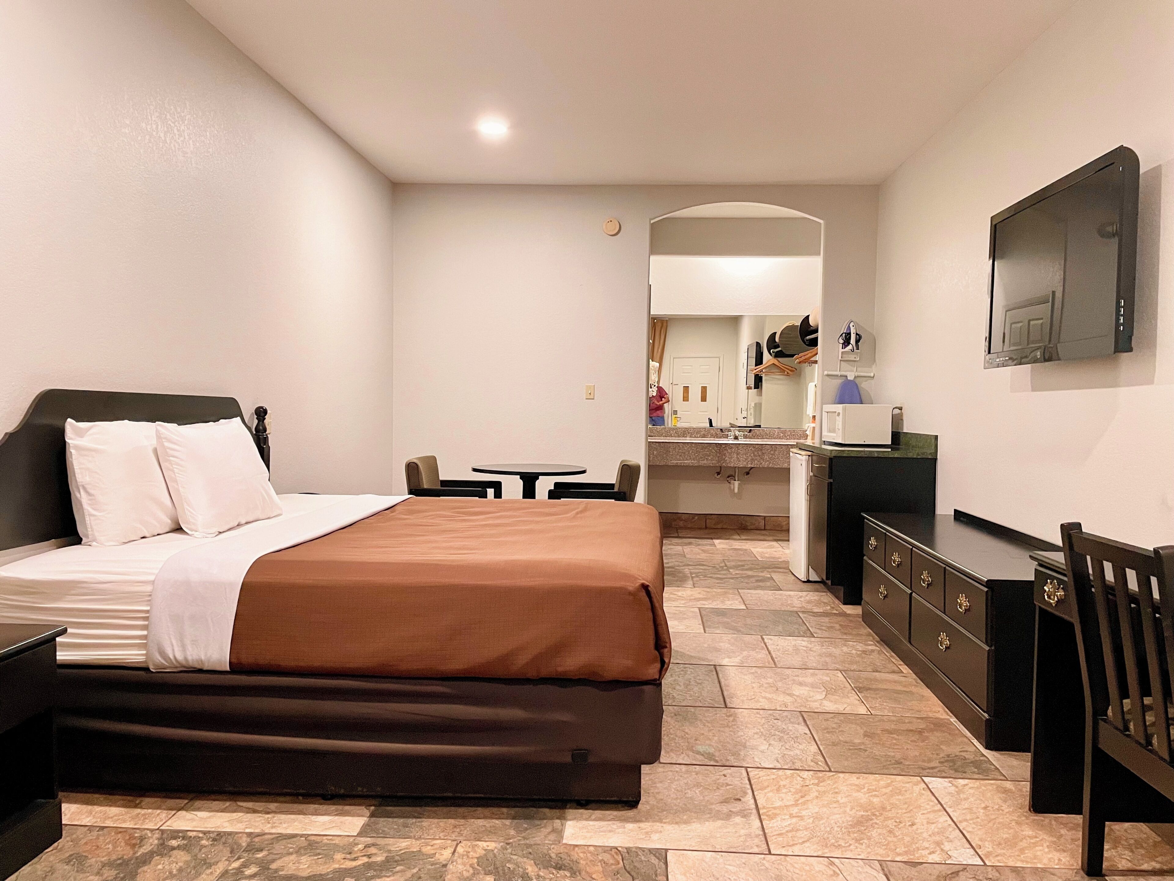Habitación de hotel con cama, escritorio, silla, mesita, espejo y televisor.