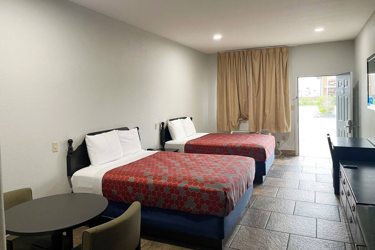 A hotel room with two beds, a small table, a chair, a desk, and a television.