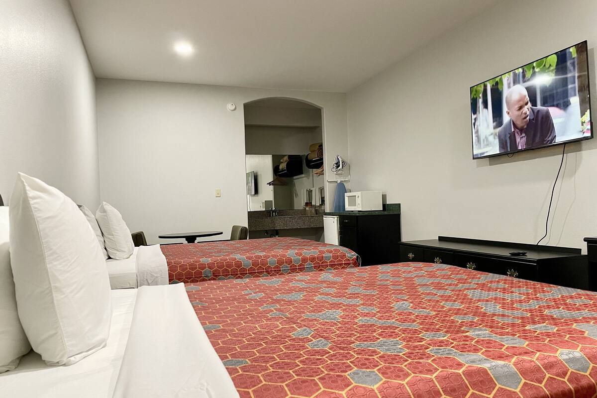 A hotel room with two beds, a TV mounted on the wall, a small kitchenette, and a mirror.