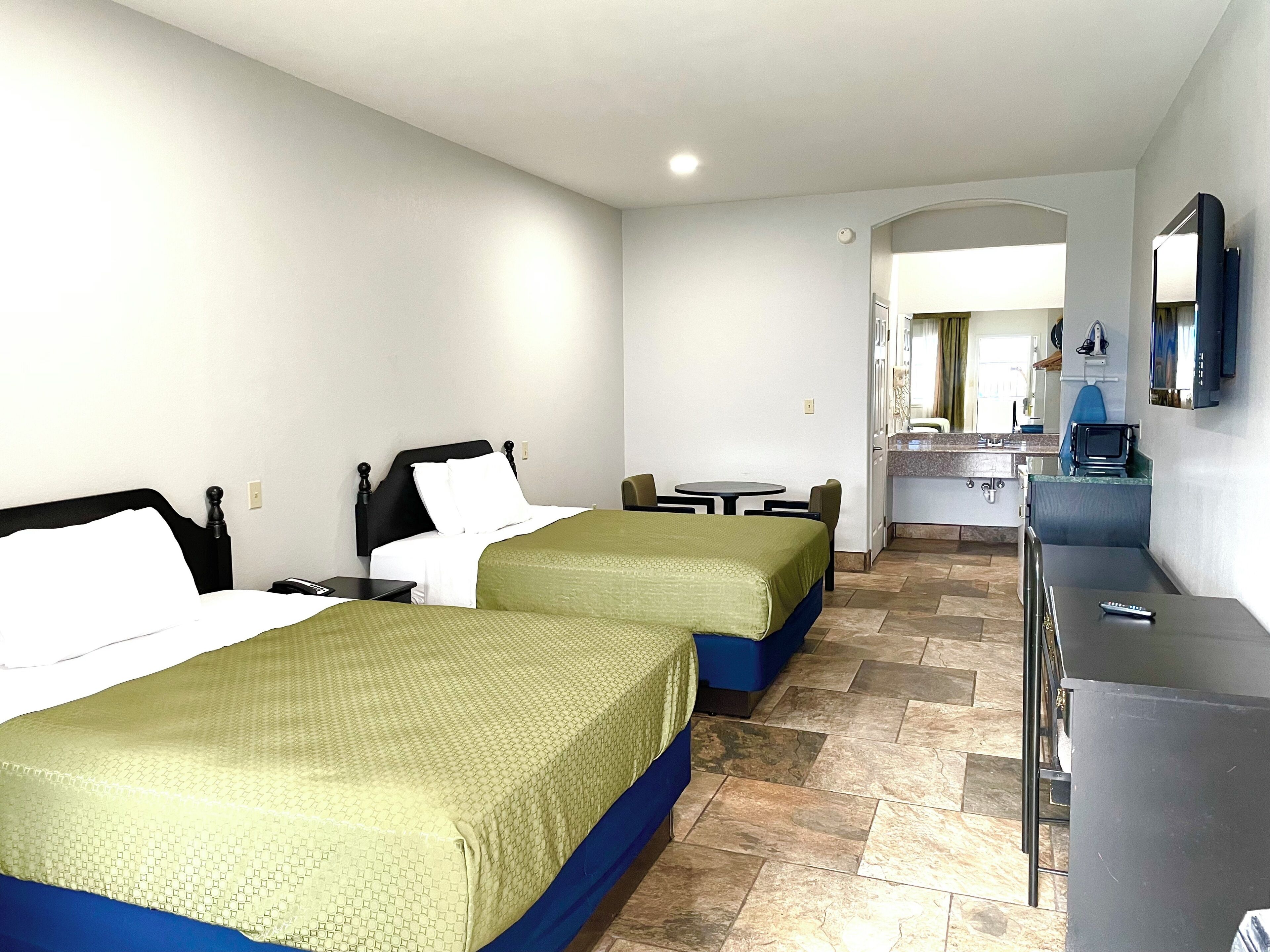 Una habitación de hotel con dos camas, una mesita, un escritorio y un kitchenette.