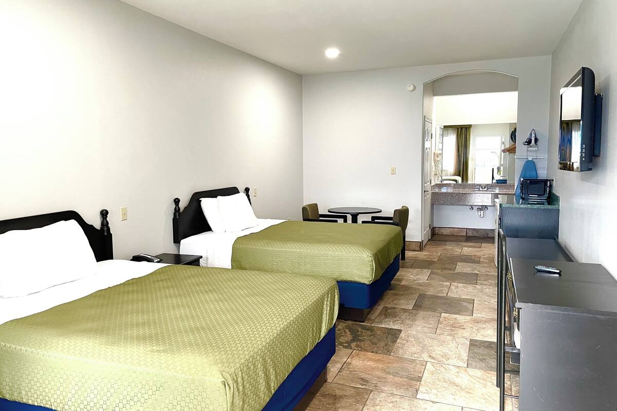 A hotel room with two beds, a small table, a desk, and a kitchenette.