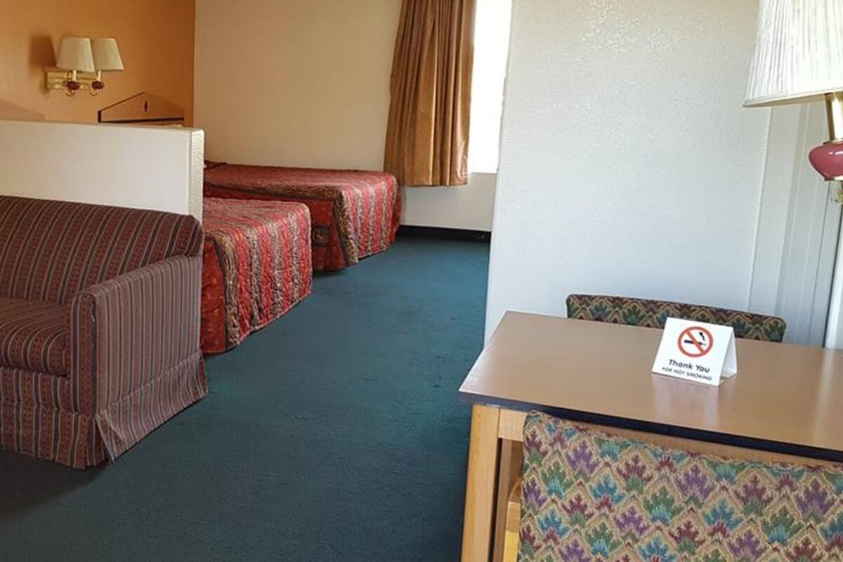 A hotel room with a sofa, two single beds, a small table, a desk, and a "Thank You" sign.