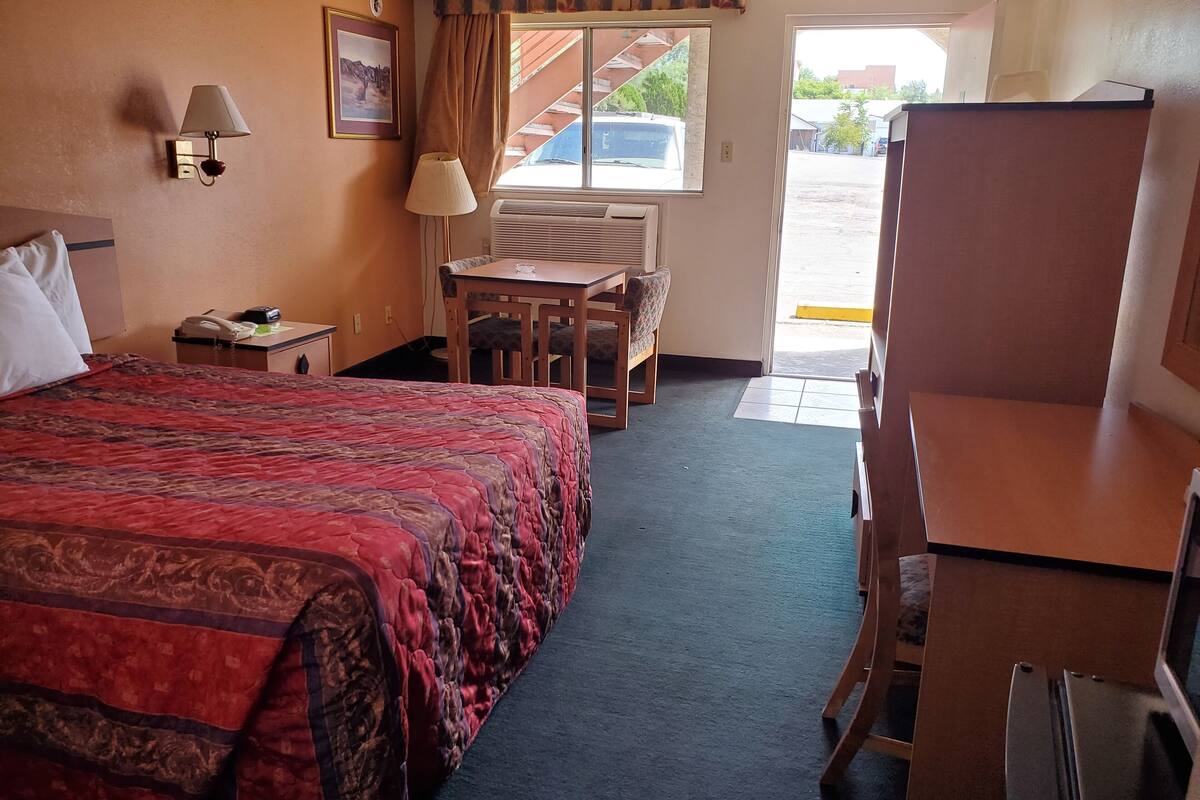A hotel room with a large bed, a desk, a chair, a lamp, and a window with a view of the outside.