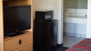 Une chambre d’hôtel équipée d’un téléviseur à écran plat, d’un réfrigérateur noir et d’un lit recouvert d’une couvre-lit à motifs.