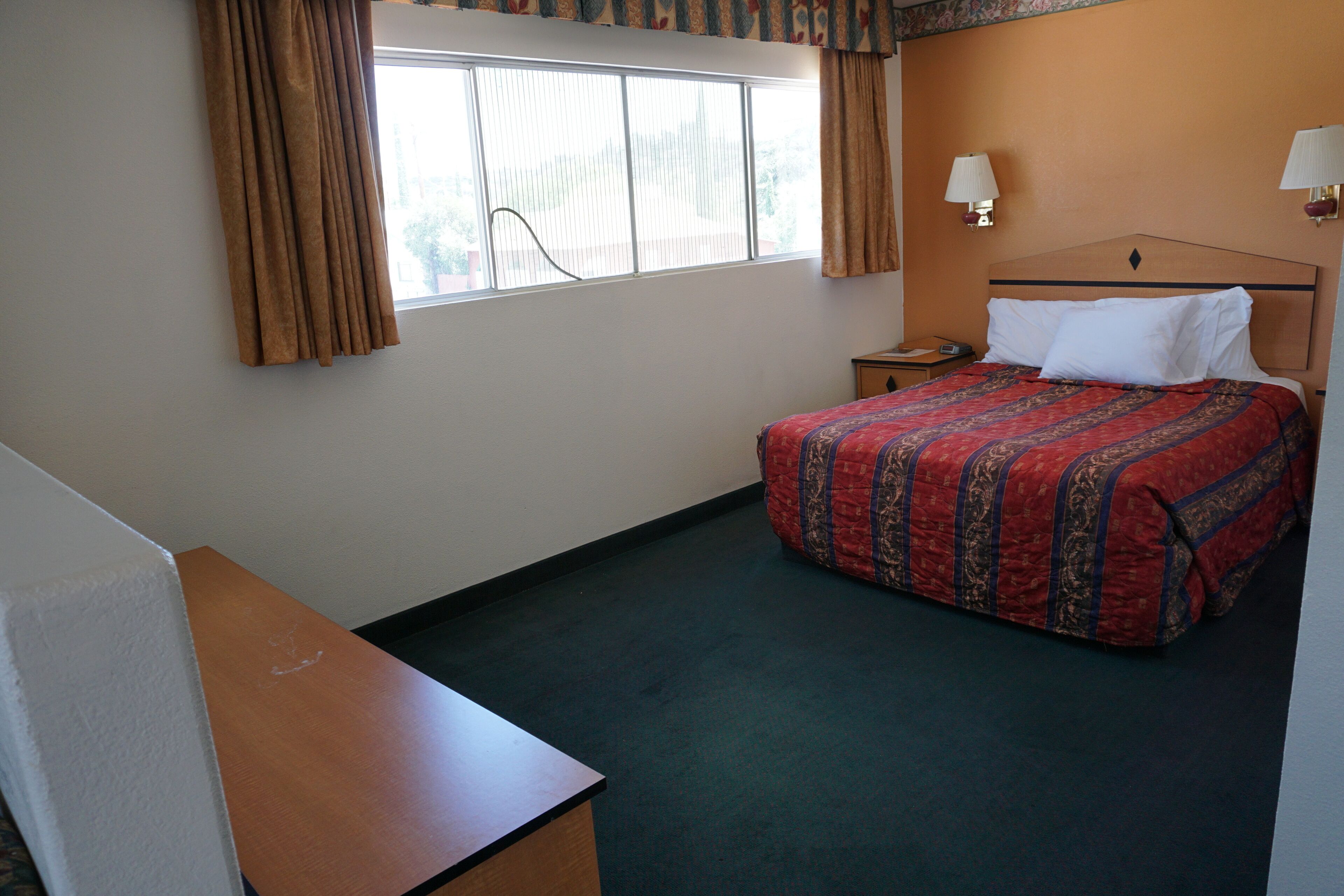 A hotel room with a bed, a nightstand, a desk, and a window with curtains.