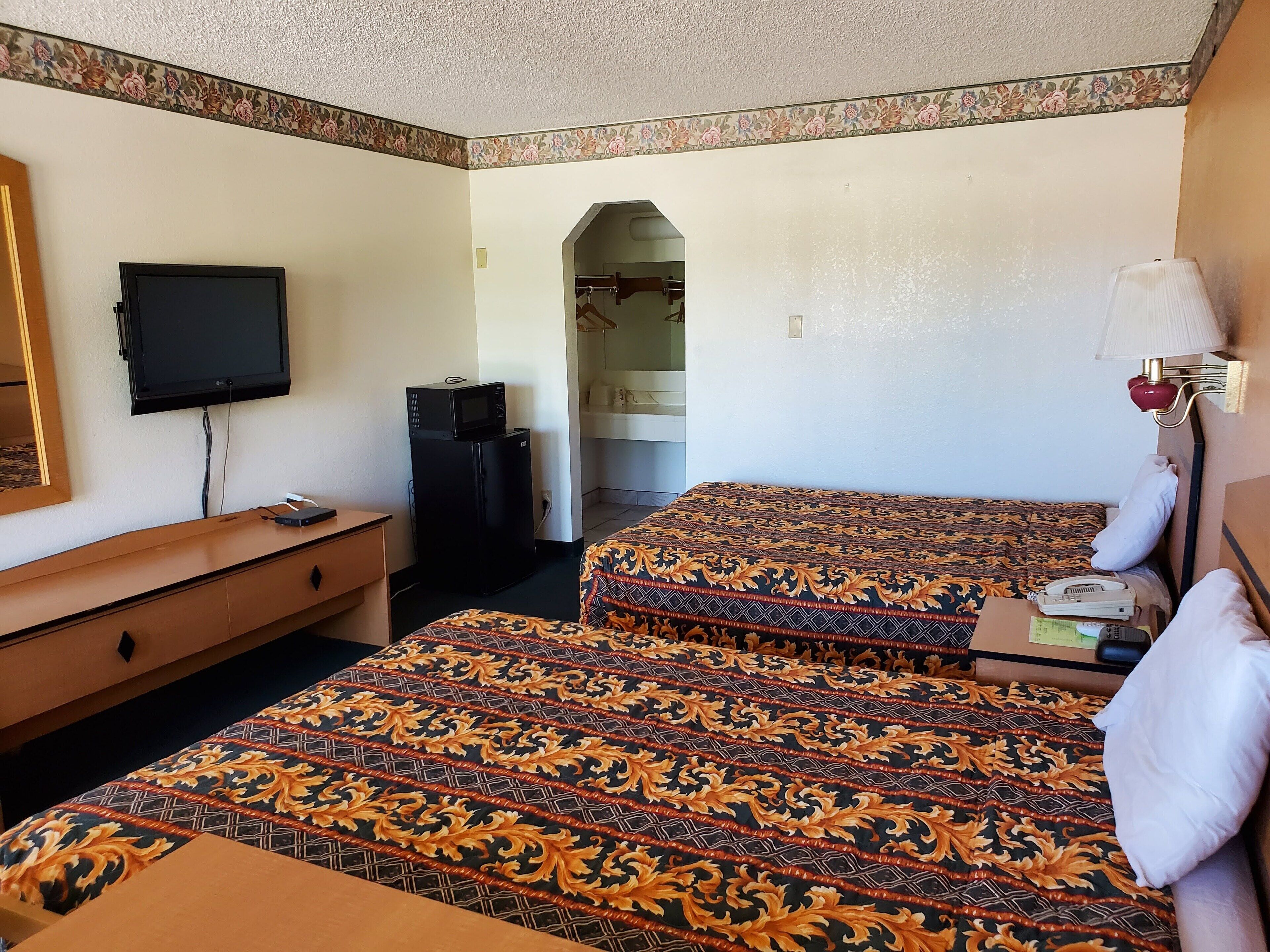 A hotel room with two beds, a desk, a television, a microwave, and a telephone.