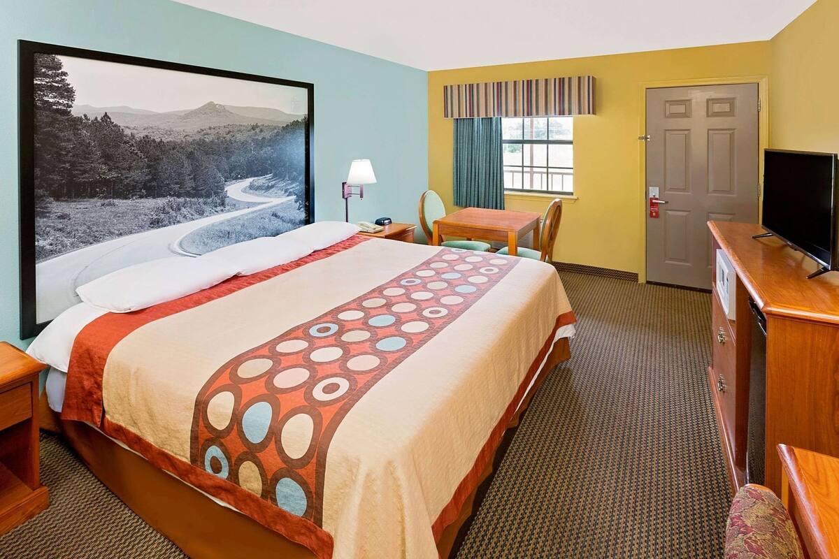 A hotel room with a bed, a desk, a chair, a television, a lamp, and a door.