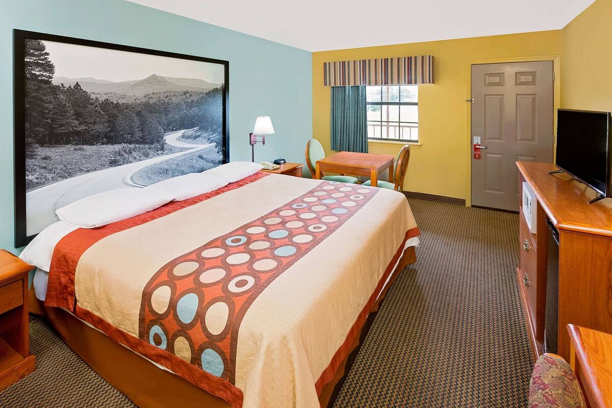 A hotel room with a large bed, a desk, a chair, a television, and a door.