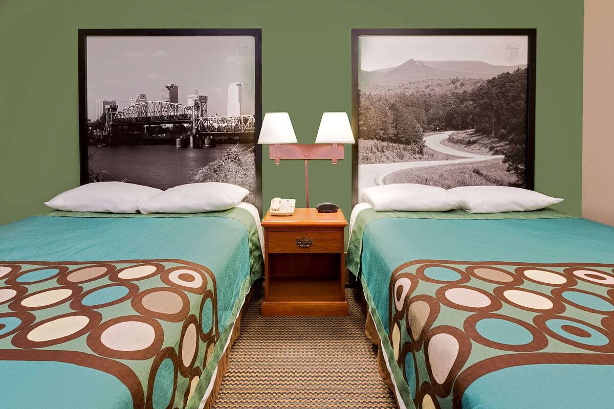 A hotel room with two beds, a nightstand with a lamp, and two framed pictures on the wall.
