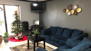 A living room with a dark blue sectional sofa, a small coffee table, a television on the wall, and a Christmas tree.